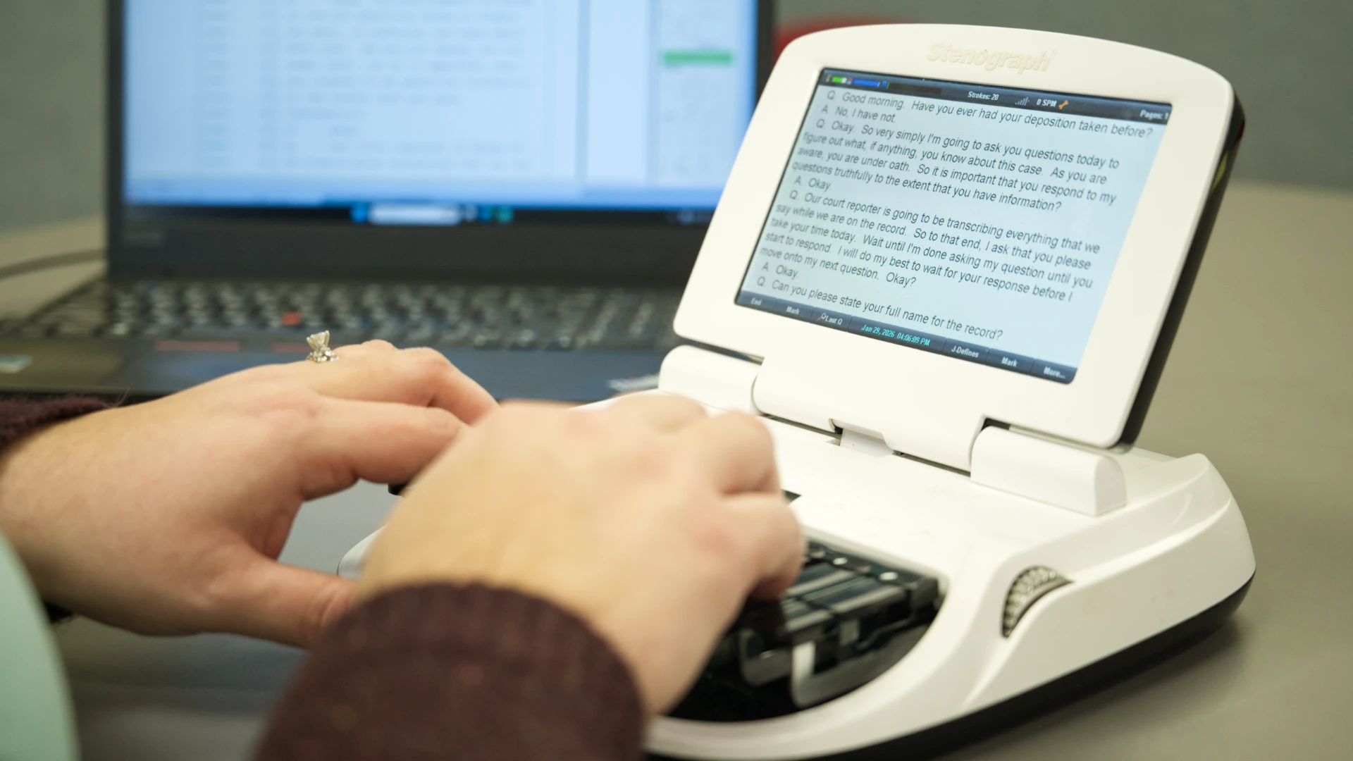 Woman stenographer typing with a laptop in the background.