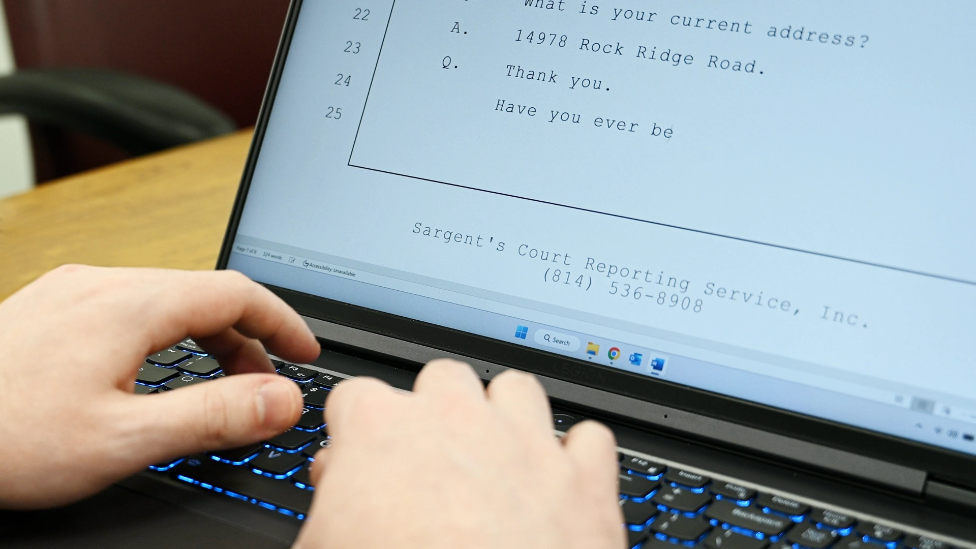 A close up of a hands typing on a laptop with a portion of the screen displaying transcription software.